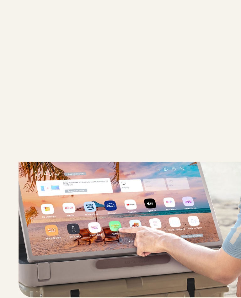 Close-up of LG StanbyME Go. The product is placed on a table, and the screen rotated horizontally. A hand is touching an icon.