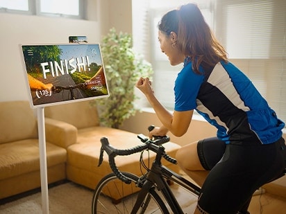 A woman is riding an indoor bicycle. She has StanbyME in front of her and the words 'finish' can be seen on the screen.
