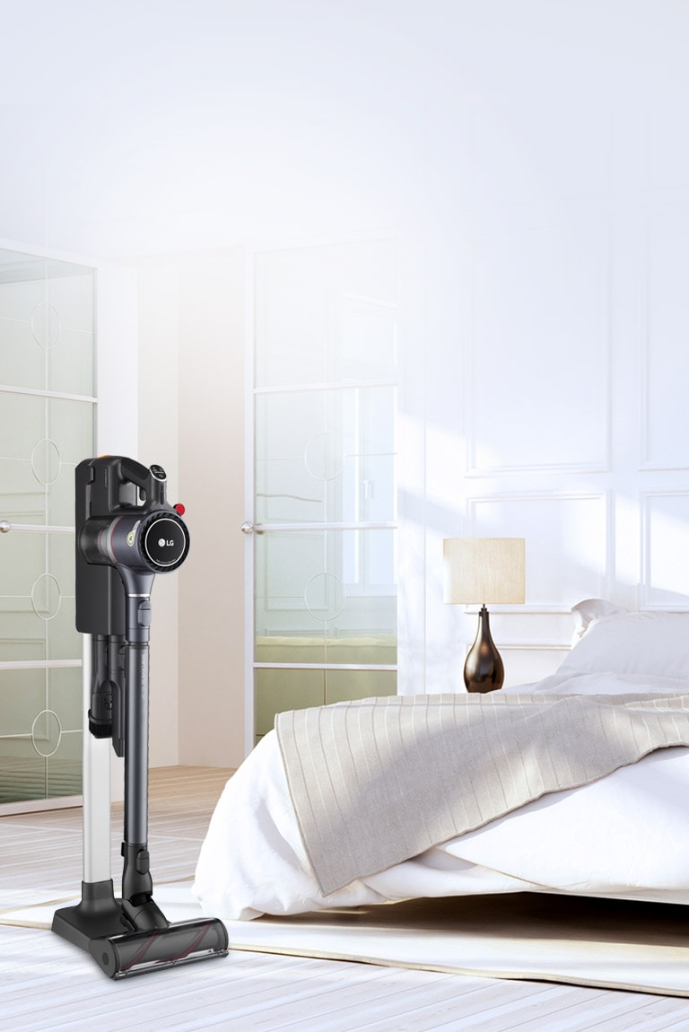 The CordZero A9 Kompressor Vacuum is in the charging stand in a bedroom next to a bed.
