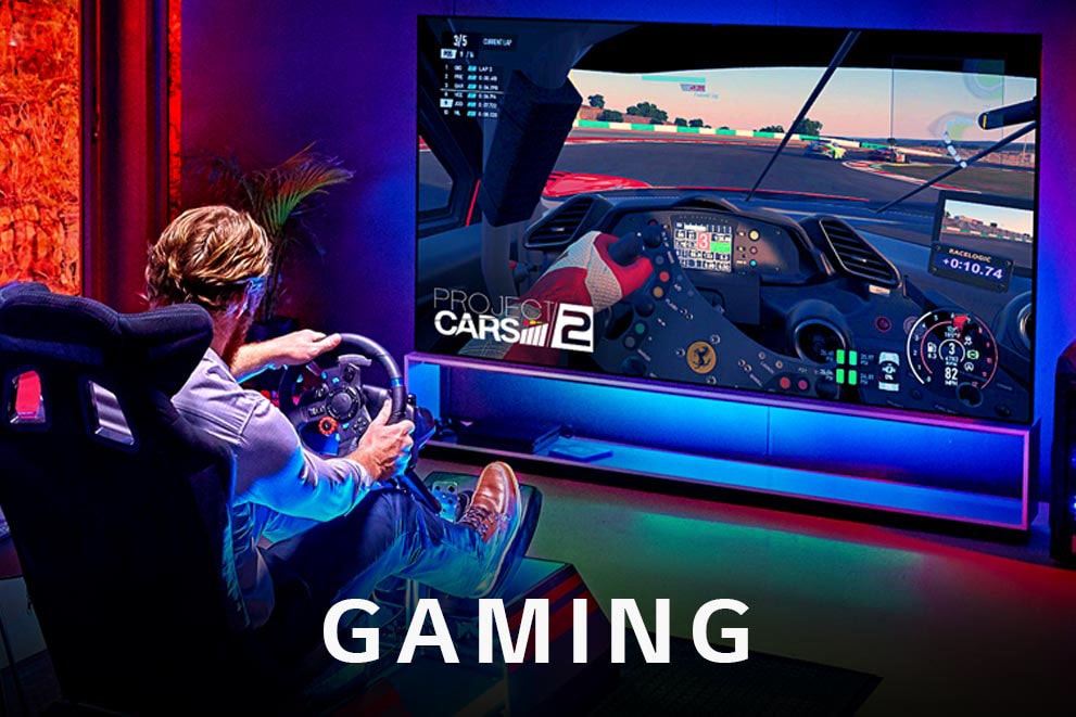 In front of a large LG OLED TV, a man is sitting on a racing seat and playing a racing game