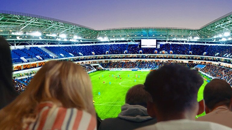 People are watching a football game with the backdrop of a view of the entire stadium on a large TV