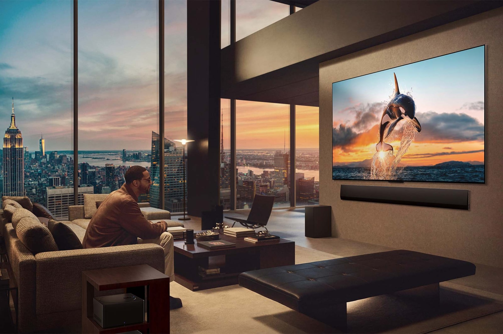 Spacious living room with a view of a cityscape. LG OLED TV is mounted on the wall with an LG Soundbar. The TV's One Wall Design allows it to be flush-fit against the wall and blend well with the space. Zero Connect Box is visible, but concealed. 
