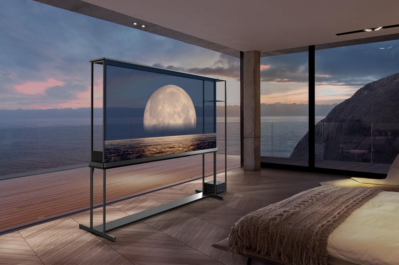 LG SIGNATURE OLED T displays a moon depicted above a shore on the transparent screen. The LG SIGNATURE OLED T sits in the middle of a room with a cliff side view that looks out to the sea. On the right is a bed and a lounge chair. 