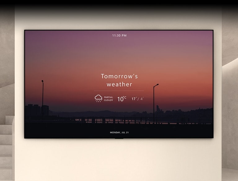 There is a large wall in the space with stairs and lighting, and a TV is hung there. Inside the TV screen, there is a sunset landscape with today's weather information.