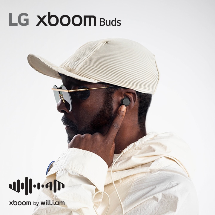 will.i.am in white outfit and sunglasses is his facing right side pointing the earbud in his ear with his left index finger.