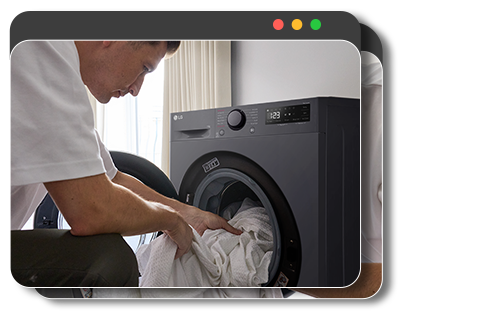 Egy férfi ruhákat tesz a mosógépbe, és okostelefonos alkalmazással figyeli a mosást.