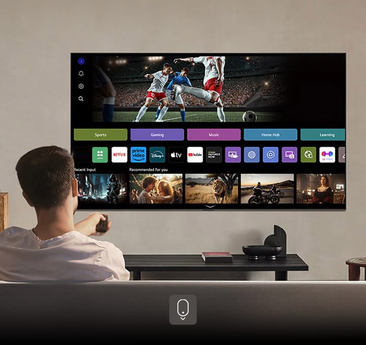 A kanapén ülő személy egy távirányítót tart a kezében. LG AI TV a falon, a képernyőn LG webOS.