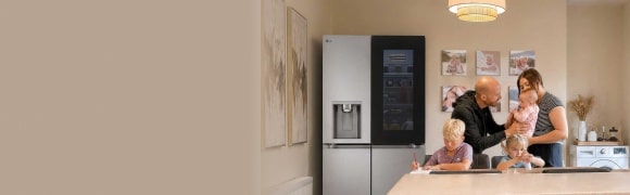 Egy család három gyermekkel egy modern konyhában, egy nagyméretű, rozsdamentes acél hűtőszekrény mellett.