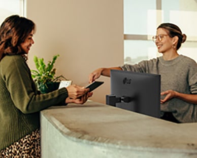 Barátságos recepciós mutatja egy hölgynek, hogy hol kell aláírni egy digitális táblagépen.	
