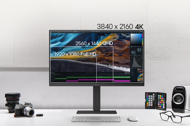 Egy asztalon lévő fehér LG-monitor elülső nézete, amely összehasonlításképpen rétegzett képernyőfelbontásokat mutat, körülötte kamerák, könyvek, színes chipek és hangszórók vannak elhelyezve.