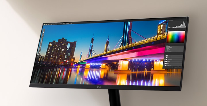 LG ultraszéles monitor, amely egy élénk éjszakai városképet jelenít meg egy fényesen megvilágított híddal és visszatükröződéssel, egy fotószerkesztő szoftver felületén, amely kiemelve a szín- és kontraszteszközöket.