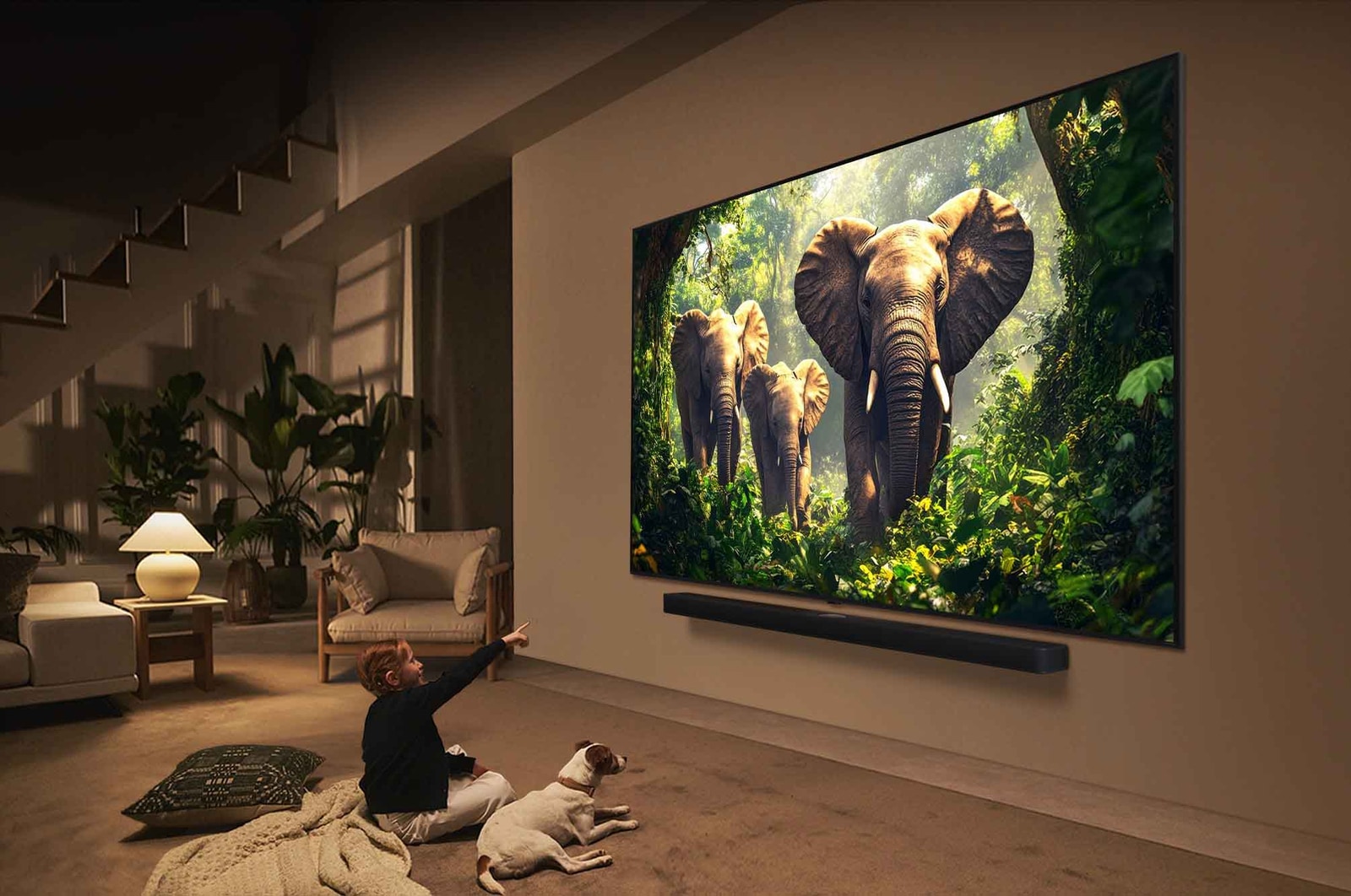 Seorang gadis dan seekor anjing duduk di depan LG QNED TV yang terpasang di dinding yang menggambarkan tiga gajah berjalan keluar di atas LG Soundbar. Judulnya membahas tentang bagaimana setiap aksi menjadi lebih mendebarkan di layar besar.