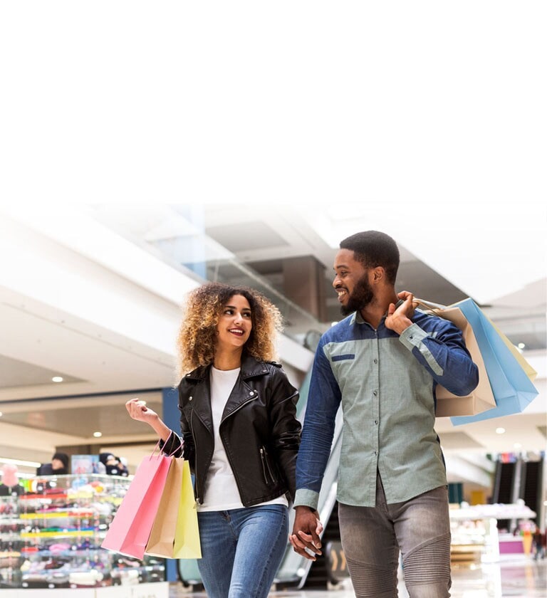 Sepasang kekasih sedang berbelanja di pusat perbelanjaan dengan tas belanja berwarna-warni.