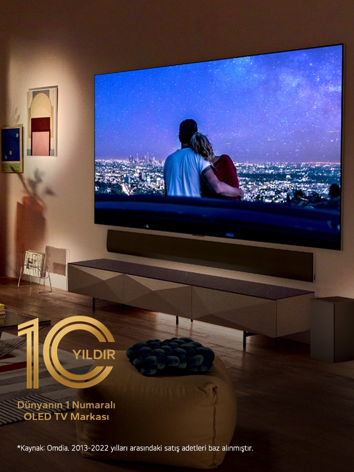 Sebuah gambar LG OLED evo G3 di dinding apartemen kota New York modern dan unik dengan adegan malam romantis yang diputar di layar. Lambang 10 Tahun TV OLED Terbaik di Dunia.