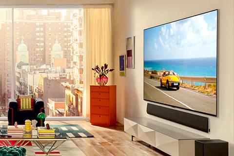 Tampilan miring LG OLED G3 di dinding apartemen dengan pemandangan kota dengan Soundbar di bawahnya.
