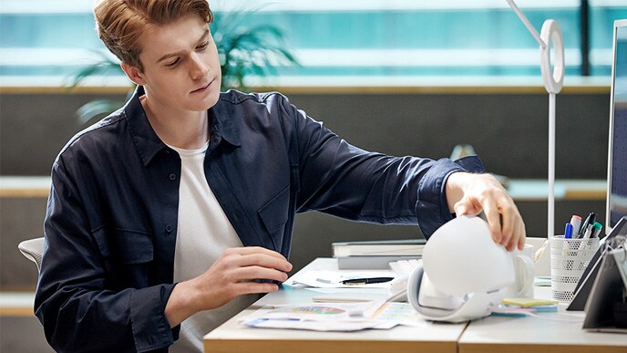 Seorang pria dengan jaket kulit duduk di meja sedang membuka PuriCare wearable case dan melihat ke dalamnya.