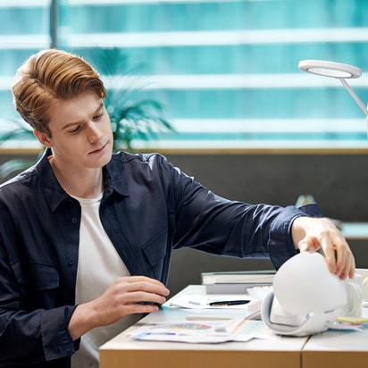 Seorang pria dengan jaket kulit duduk di meja sedang membuka PuriCare wearable case dan melihat ke dalamnya.