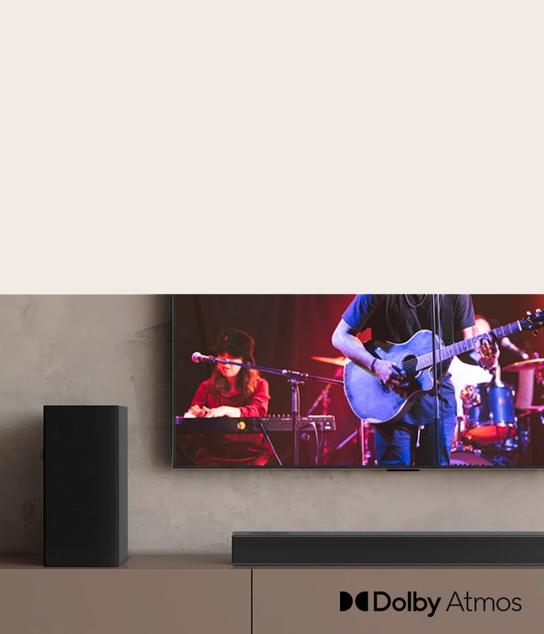 TV LG menampilkan konser, dan LG Sound Bar ditempatkan di bawah TV LG. Di sebelah kiri, speaker belakang berada di rak berwarna cokelat.