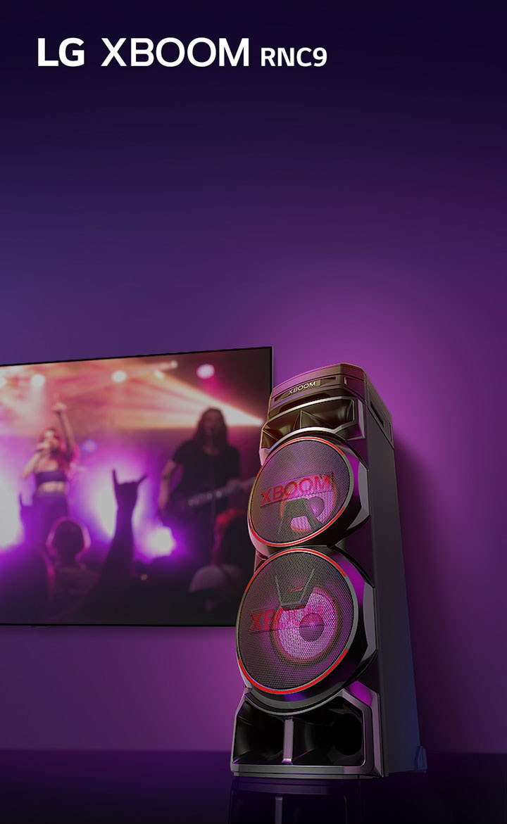 Sudut pandang rendah dari sisi kanan LG XBOOM RNC9 dengan latar belakang ungu. Lampu XBOOM juga berwarna ungu. Dan layar TV menghasilkan adegan konser