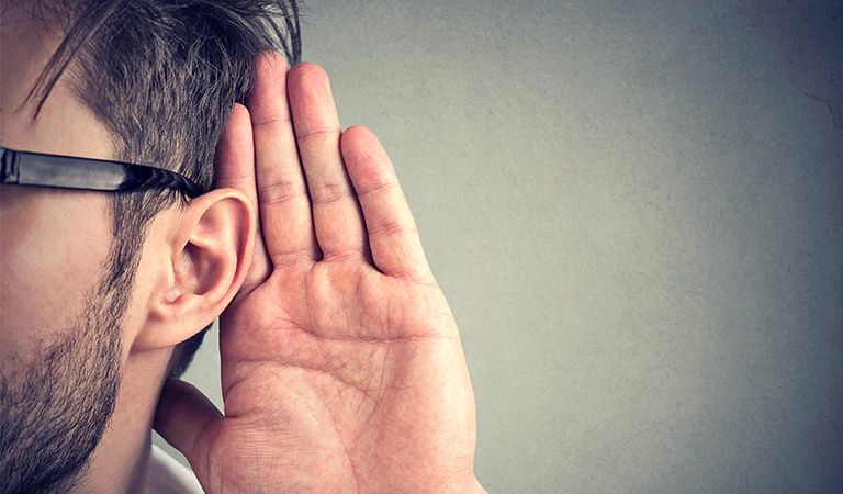 A person putting his had by his ear to listen carefully