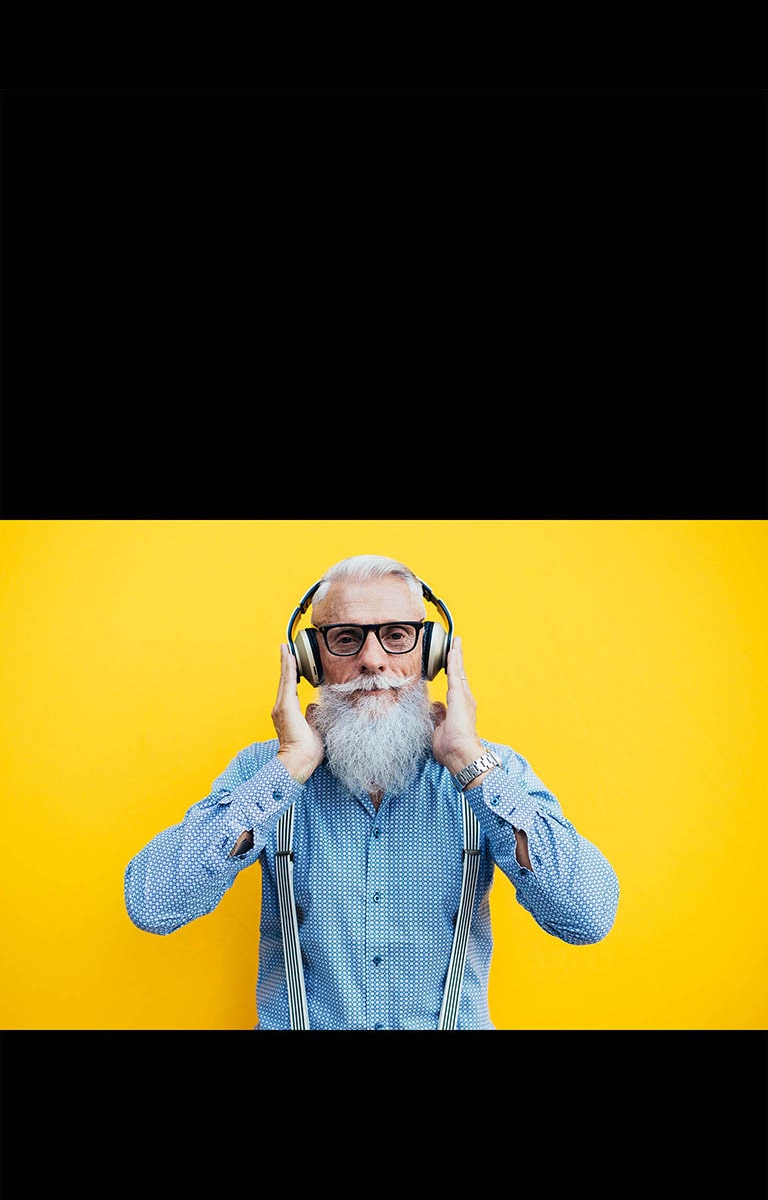 Seorang kakek berdiri di depan tembok berwarna kuning – sedang mengenakan headset.