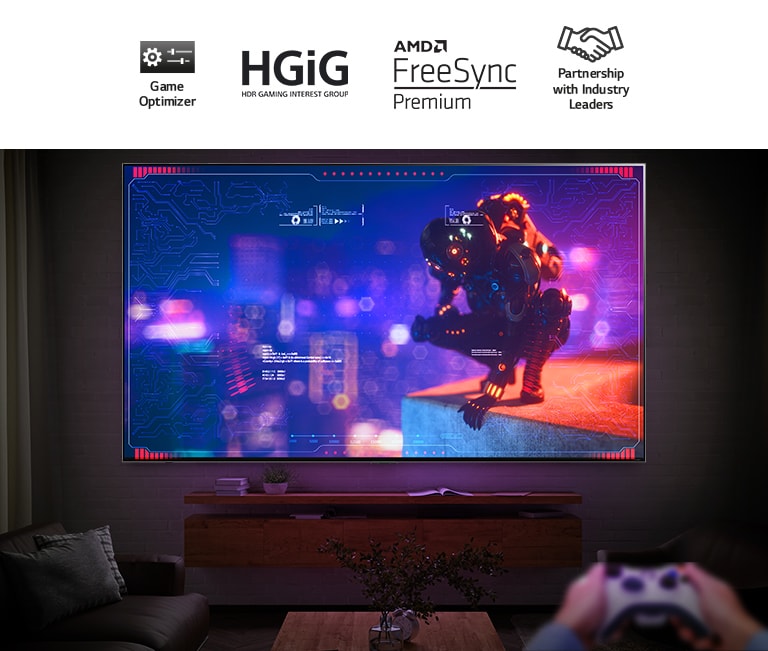 TV berlayar besar dipasang di dinding dalam ruangan yang gelap. Layarnya menayangkan karakter fiksi ilmiah di tepi sebuah bangunan. Tangan sedang memegang game controller di sudut kanan bawah.