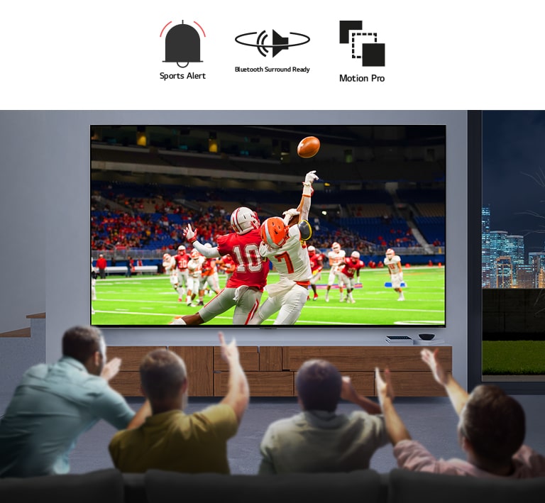 Tampak belakang empat orang pria sedang menonton pertandingan sepak bola di LG QNED MiniLED TV layar besar yang terpasang di dinding.