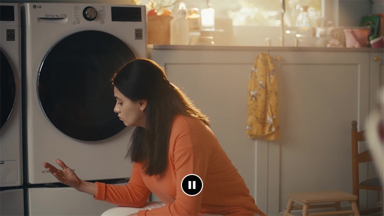 Seorang wanita sedang duduk di depan mesin cuci sambil memandangi tangannya yang basah