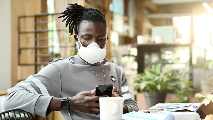 Seorang laki-laki African American sedang melihat handphone, dengan LG PuriCare™ Wearable Air Purifier hitam yang menyala