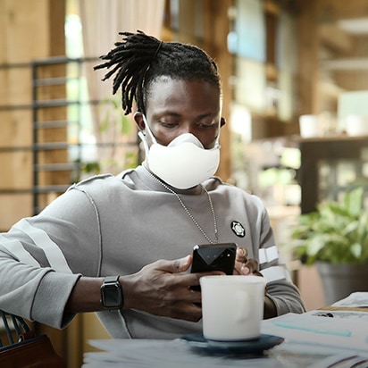 Seorang laki-laki African American sedang melihat handphone, dengan LG PuriCare™ Wearable Air Purifier hitam yang menyala