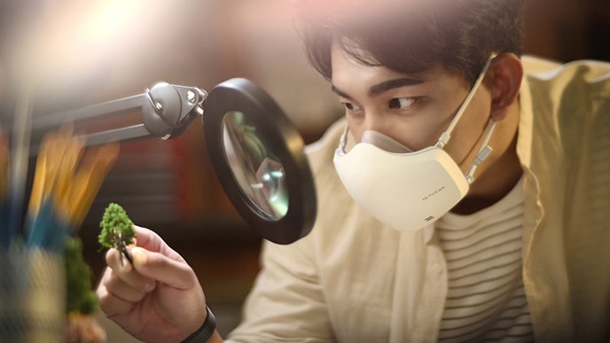 Seorang pria Asia sedang melihat sesuai melalui mikroskop sembari menggunakan LG PuriCare™ Wearable Air Purifier yang menyala