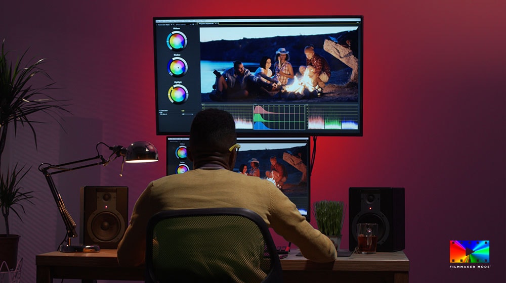 Seorang pembuat film sedang berada di meja menggunakan dua monitor untuk mengedit warna video.