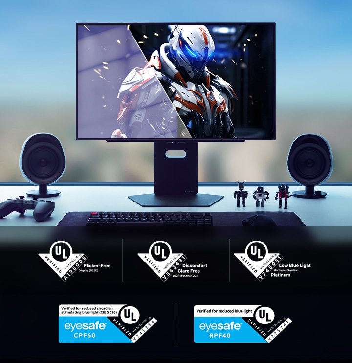 Sebuah setup gaming desktop futuristik dengan monitor besar yang menampilkan karakter berarmor bertema fiksi ilmiah. Meja tersebut dilengkapi dengan kontroler, speaker, keyboard mekanis, dan figur aksi. Sertifikasi UL dan Eyesafe yang menunjukkan fitur bebas kedipan, bebas silau, cahaya biru rendah, dan keamanan mata ditampilkan di bagian bawah gambar.	