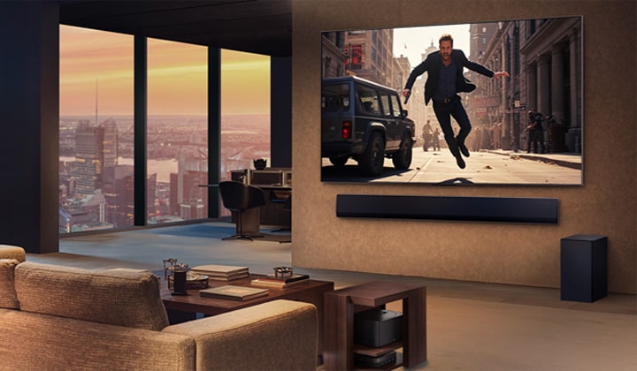 High-end stylish living room in a high-rise apartment. LG True Wireless TV and Soundbar are wall-mounted. A movie is playing on the TV screen. There are no wires in sight. The Zero Connect Box is hidden underneath a side table. 