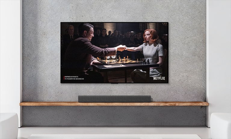 A soundbar and TV are in a white living room. A woman and a man are playing chess on TV screen.