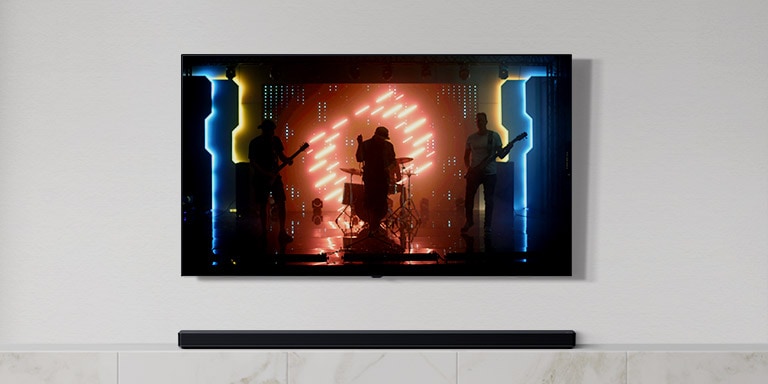 There is a TV and a soundbar in white living room. A group of band playing instruments and singing song on a TV screen. (play the video)