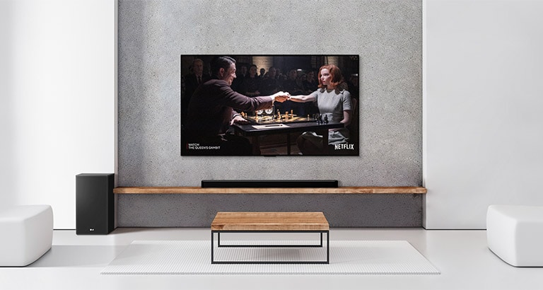 A set of 2 rear speakers, subwoofer, and a soundbar, and TV are in a white living room. A woman and a man are playing chess on TV screen.