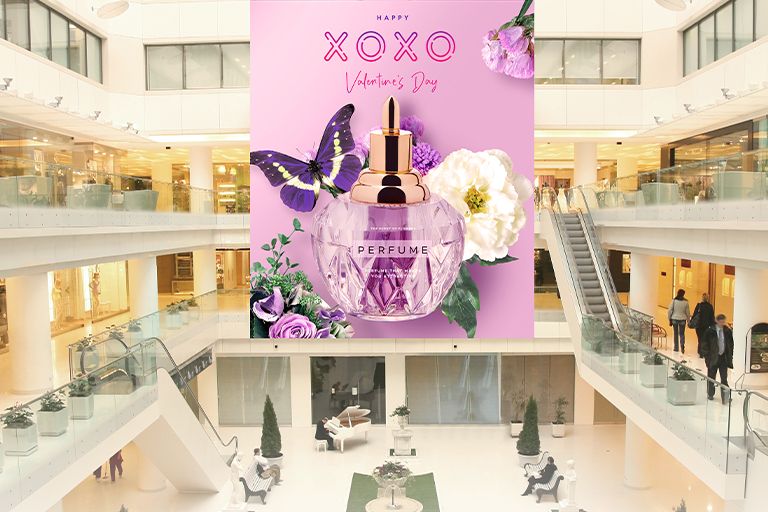 There are large LED displays installed across three floors of a large shopping mall, prominently showcasing perfume advertisements.