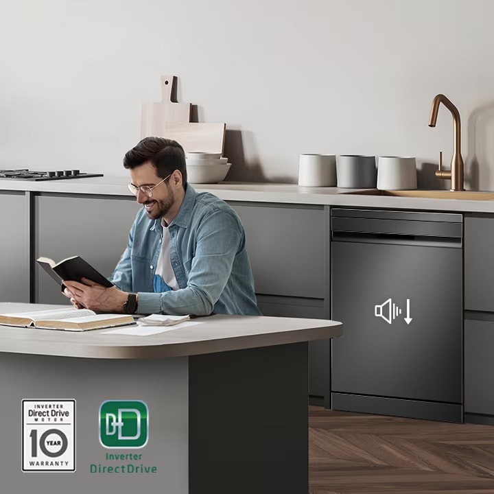 A man reading a book near an operation dishwasher, with the Inverter DirectDrive and 10-year Warranty marks displayed