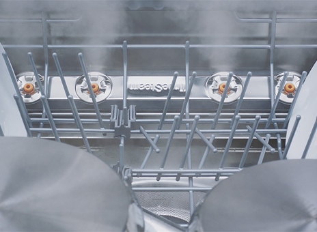 Close-up of dishes and glasses being steam-washed inside dishwasher.