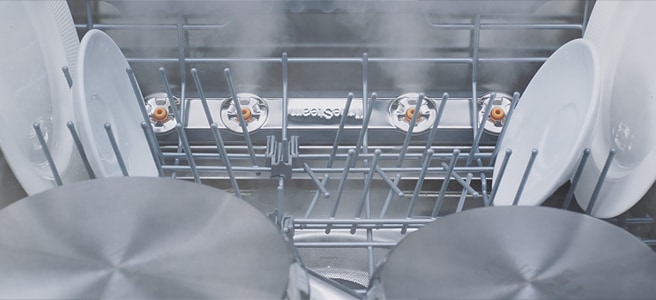 Close-up of dishes and glasses being steam-washed inside dishwasher.