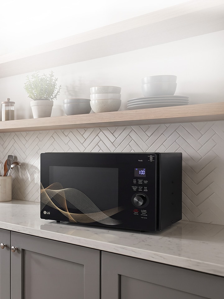 A silver countertop microwave sits in a modern kitchen with a gray stone backsplash, a sink, and a built-in oven.