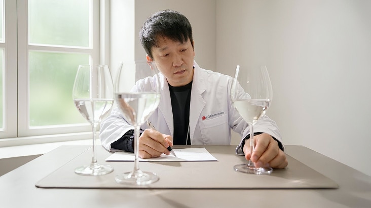 LG Electronics researcher in a white lab coat evaluating water taste using wine glasses in a bright room