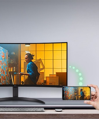 A monitor is placed on the table, and to the right, a phone displaying the same screen as the monitor is visible.