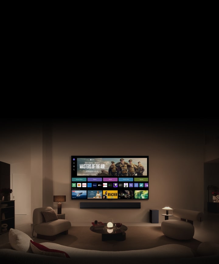 A close-up of an LG TV screen showing WebOS the buttons Home Office, Game, and Music over a banner for Masters of the Air zooms out to show the TV mounted on a wall in a living room. The following logos are displayed on the TV screen in the image: LG Channels, Netflix, Prime Video, Disney TV, Apple TV, YouTube, Spotify, Twitch, GeForce Now and Udemy.