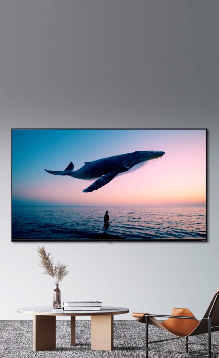 Big whale and a woman is diaplayed in the TV, which is hanging on the wall in the room with orange single sofa and round table.