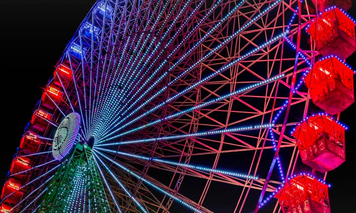 Un ruota panoramica illuminata di notte, con scintille colorate che partono dal lato sinistro dello schermo e si spostano attraverso di esso. Mentre le scintille colorate passano, lo schermo transita da sbiadito a colori vivaci e luminosi