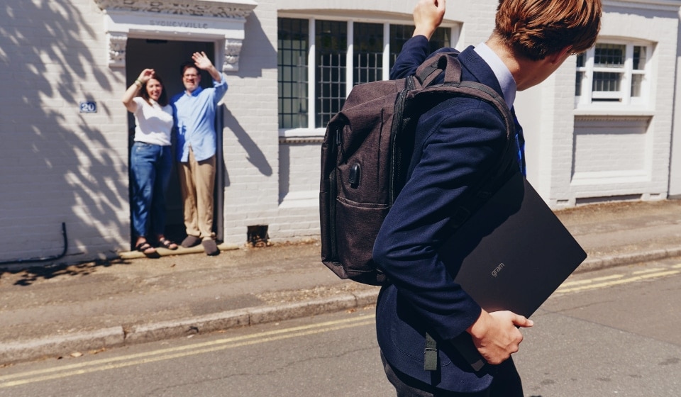 Studente con laptop e zaino che saluta i genitori prima di andare a scuola.