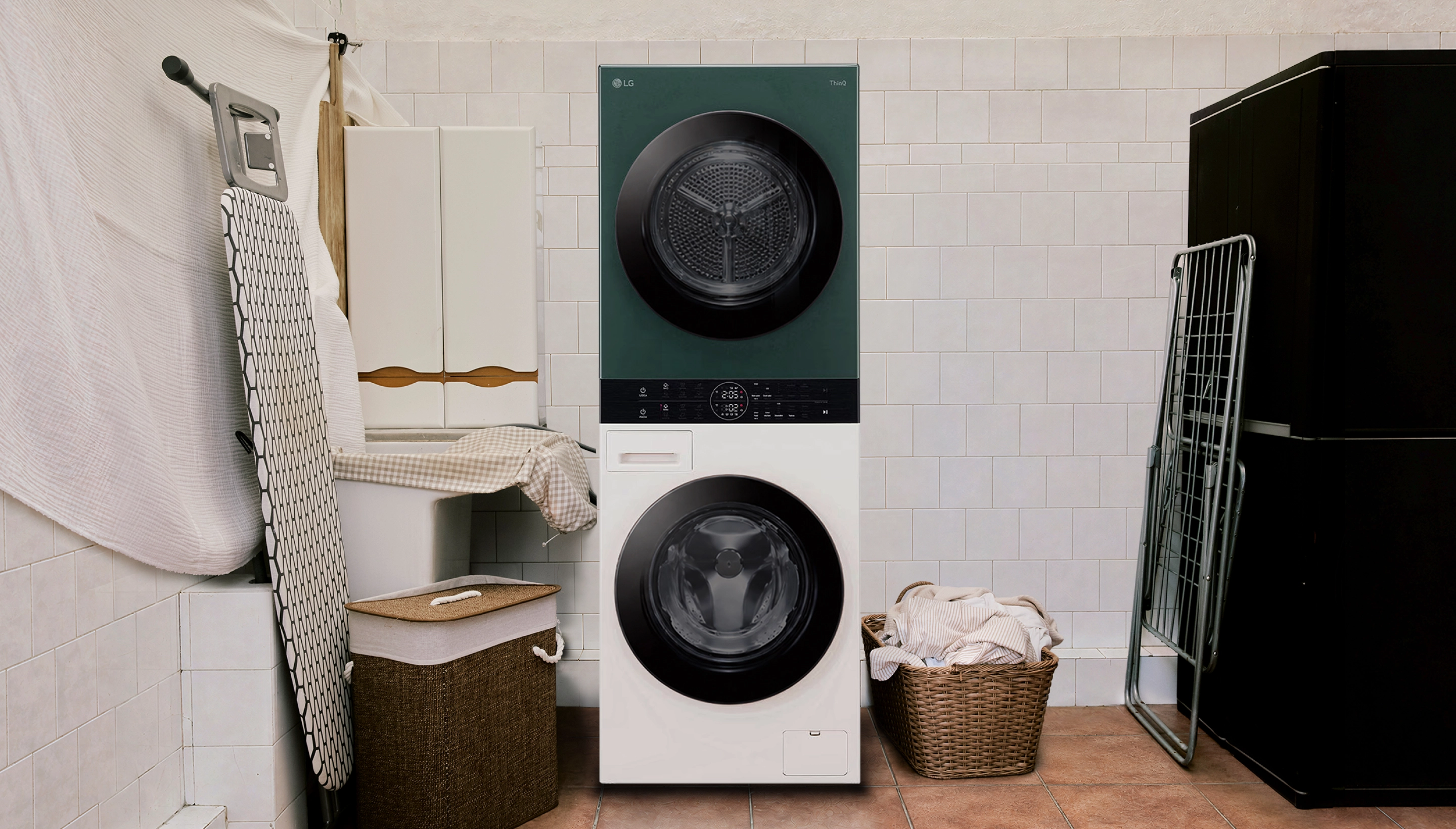 Una LG WashTower, con lavatrice e asciugatrice sovrapposte, in una lavanderia piastrellata, accanto a un cesto della biancheria pieno di asciugamani.