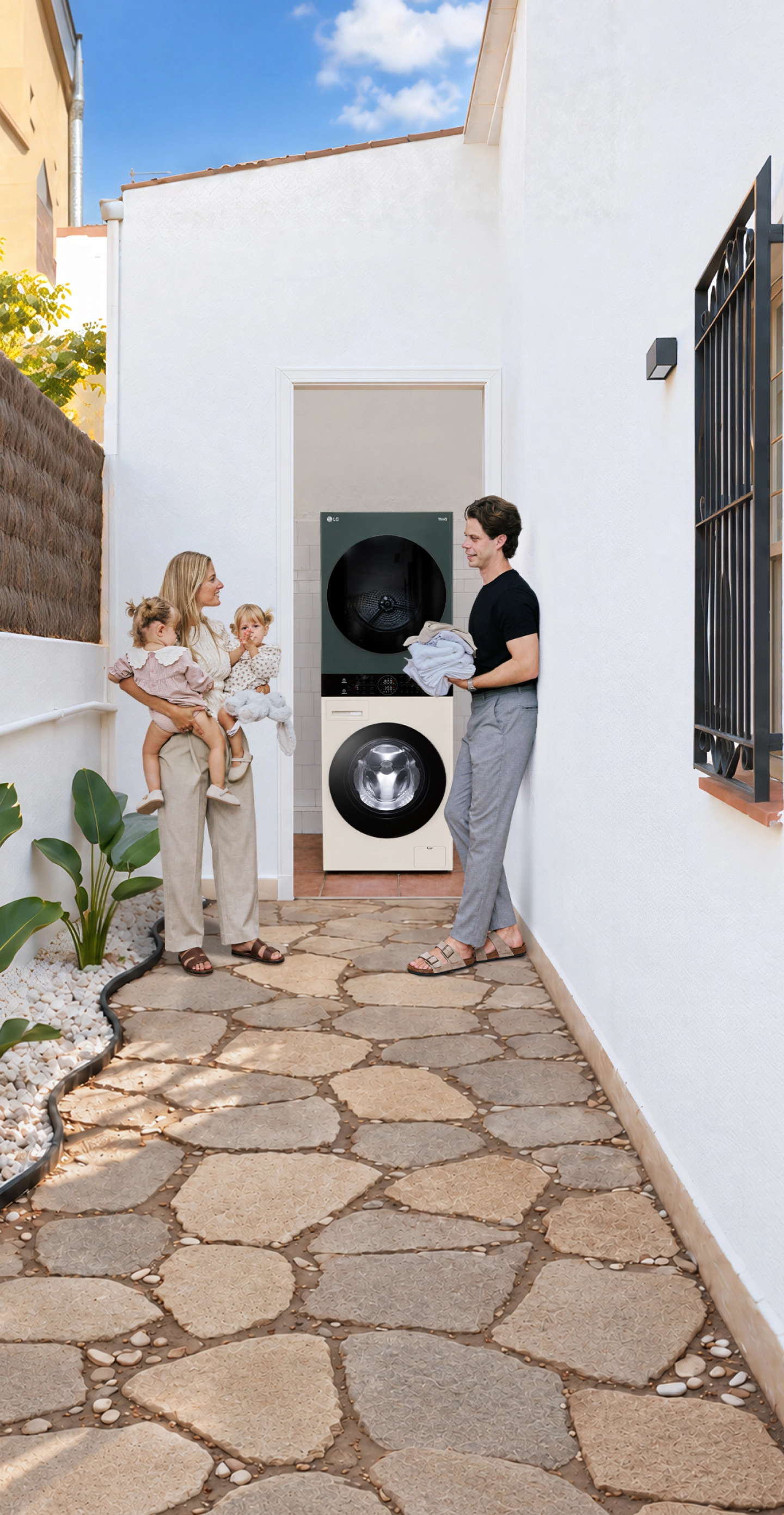 Una famiglia con due gemelli piccoli in piedi in un corridoio esterno dalle pareti bianche, accanto a una lavatrice e un'asciugatrice LG sovrapposte.